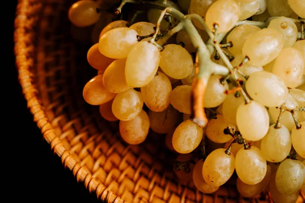 Koyu bir arka planda dokuma sepetinde duran olgun sarı üzümler.
