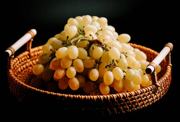 Olgun yeşil üzümler, koyu bir arka planda dokuma sepetinde dizilmiş.