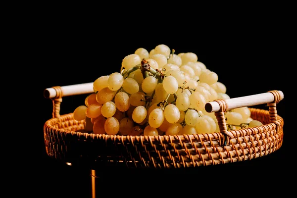 Taze toplanmış olgun üzümler, koyu bir arka planda dokuma sepetinde sergilenir.