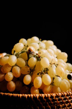 Olgun üzümler dokuma sepetinde koyu arka planda taze görünüşlerini sergiliyorlar.