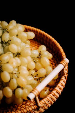 Örülmüş sepetteki taze üzümler koyu bir arka planda hasat ve tüketime hazır.