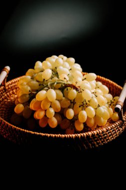 Olgun üzümler, yumuşak ışığın altında, karanlık bir ortamda örülmüş sepetin içinde.