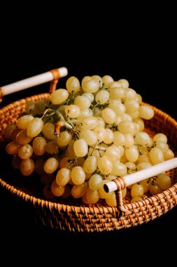 Taze olgun üzümler koyu bir arka planda dokuma sepetinde sergilenir.