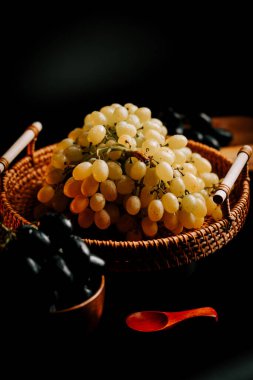 Olgun yeşil ve siyah üzümler dokunmuş sepetin içinde çarpıcı bir ışıkla yakalandı.