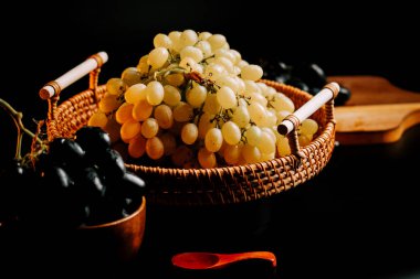 Bir sepetin içinde olgunlaşmış üzümler. Karanlık bir ortamda taze meyve sergiliyorlar.