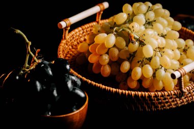 Olgun üzümler dokuma sepetinde, sanatsal olarak koyu bir arkaplanda dizilmiş.