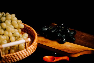 Tahta kesme tahtasının yanında dokuma sepetinde taze olgun üzümler.