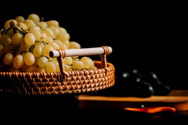 Örülmüş bir sepetin içindeki olgun üzümler koyu arkaplan ve zıt renkler