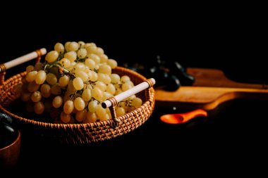 Yumuşak ışıklandırmanın altında ahşap bir arka planı olan dokuma sepetindeki olgun üzümler.