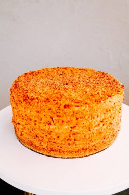 Minimalist bir ortamda beyaz bir standın üzerinde desenli bir kırıntı olan parlak turuncu pasta.