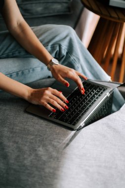 Person typing on a laptop while sitting on a sofa in casual clothes during the day