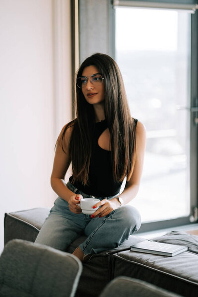 Young woman enjoying coffee while sitting on a couch in a modern apartment