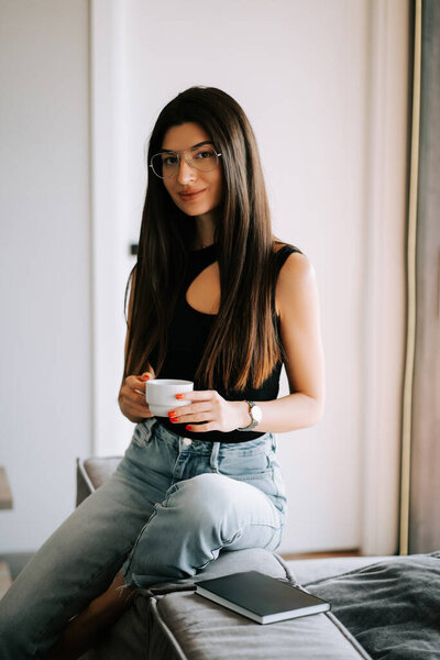 Young woman enjoys coffee while sitting on a couch in a bright modern setting