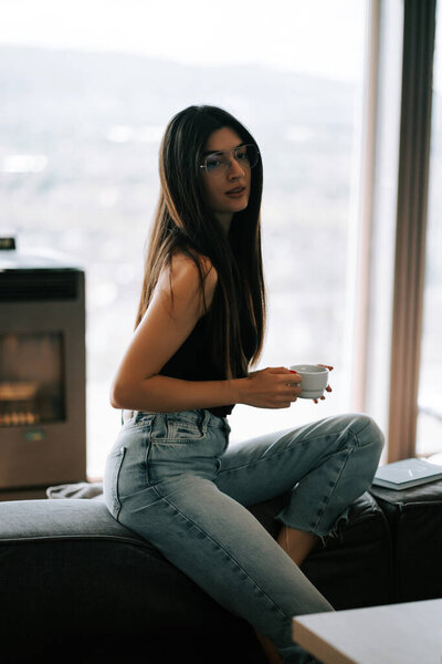 Young woman enjoying coffee in modern apartment with scenic view during daytime