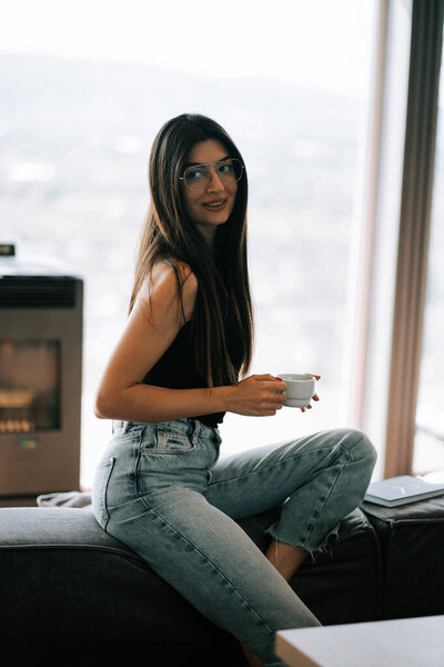 Woman enjoying coffee in modern living room with mountain view, afternoon relaxation