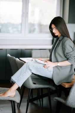 Gündüz vakti modern bir mutfak ortamında yüksek bir sandalyeye oturmuş kitap okuyan bir kadın.