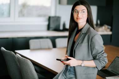 Gündüz vakti akıllı telefonunu kullanarak modern ofis ortamında çalışan profesyonel bir genç kadın.