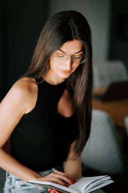 Gün ışığında, rahat bir evde kitap okuyan genç bir kadın.