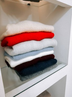 Modern bir yerde rafa dizilmiş renkli süveter yığını.