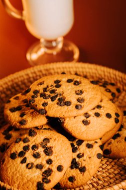 Sıcak çikolata parçacıklı kurabiyeler bir bardak sütle sıcak bir masada.