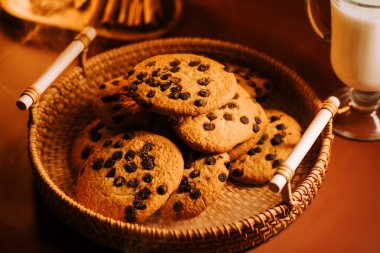 Bir bardak sütle örülmüş sepetin üzerinde taze pişmiş çikolatalı kurabiyeler.