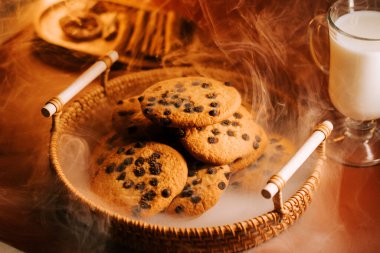 Sıcak bir masada soğuk sütle servis edilen taze pişmiş çikolatalı kurabiyeler.