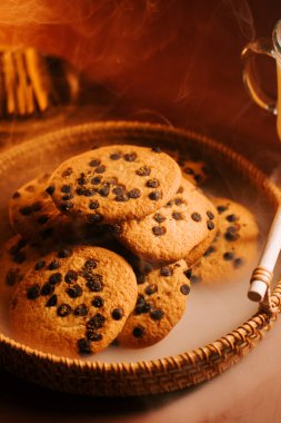 Sıcak bir ortamda buharı yükselen örülmüş tepside lezzetli çikolatalı kurabiyeler.