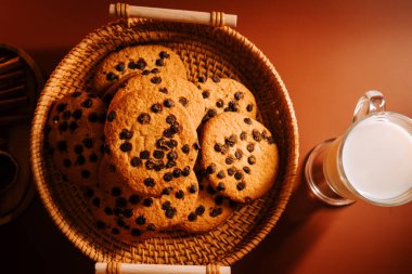 Tahta bir masada soğuk sütle taze pişmiş çikolatalı kurabiyeler.