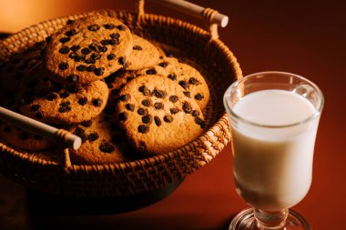 Sıcak akşam ışığında bir bardak sütle servis edilen taze pişmiş çikolatalı kurabiyeler.