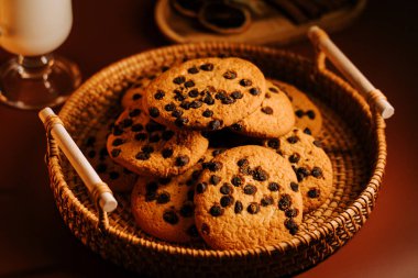 Yakınlarda bir bardak sütle dokuma sepetinde taze pişmiş çikolatalı kurabiyeler servis ediliyor.