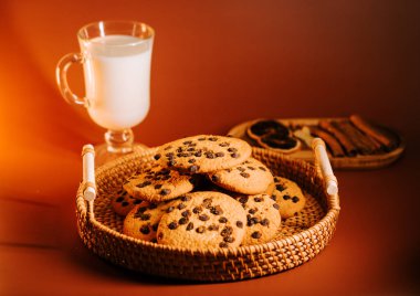 Sıcak ahşap bir yüzey üzerinde taze pişmiş çikolatalı kurabiye ve bir bardak süt.