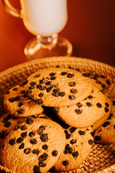 Sıcak çikolata parçacıklı kurabiyeler bir bardak sütle sıcak bir masada.