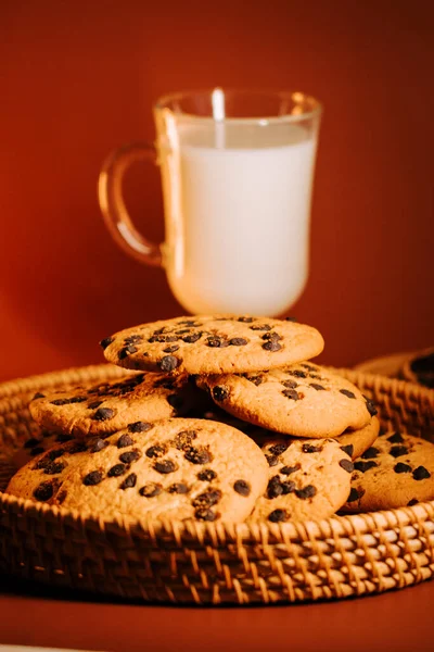 Sıcak arka planda bir bardak sütle taze pişmiş çikolatalı kurabiyeler.