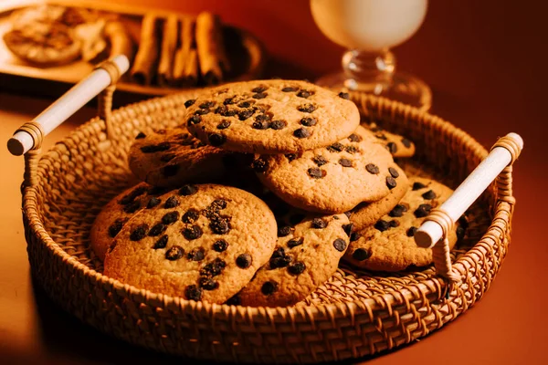 Sıcak çikolata parçacıklı kurabiyeler örülmüş sepetin içinde, konforlu ortamda bir bardak sütle.