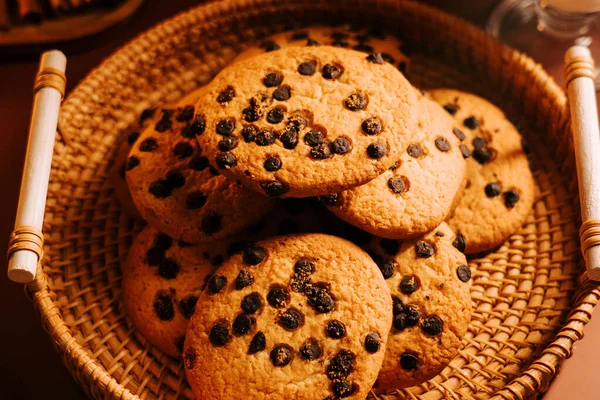 Tahta bir masanın üzerinde örülmüş sepetin içinde taze pişmiş çikolatalı kurabiyeler.
