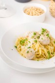Špagety s smetanové kuřecí masové kuličky, podávané na bílý talíř s piniovými oříšky