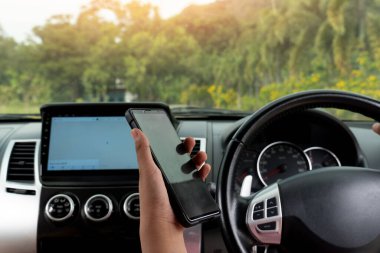 Bir şey aramak için elinde smaprtphone var. Smaprtphone ekranı siyahtı. Arabanın içinde konsol ve direksiyon gözünün önünde oturuyor. Yeşil orman geçmişi bulanık..