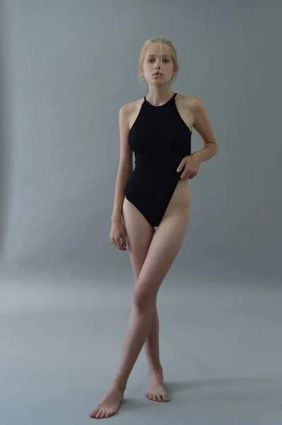 Дівчина в чорному купальнику з білим волоссям позує в студії на сірому фоні — стокове фото