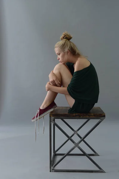 Fille en pyjama de soie vert avec décolleté posant sur une chaise dans le studio sur un fond gris — Photo