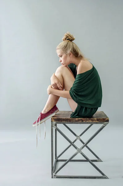 Fille en pyjama de soie vert avec décolleté posant sur une chaise dans le studio sur un fond gris — Photo