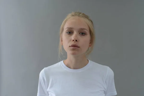Ragazza in t-shirt bianca mostra emozioni in Studio su sfondo grigio Immagine Stock