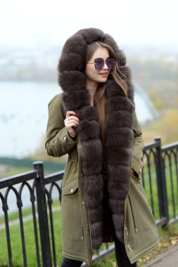 Yeşil ceketli bir kız bardaklarda göl kenarında poz bir kürk yakalı