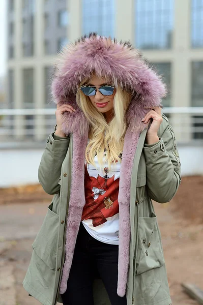 girl in down jacket with fur posing in the city on the background of glass houses