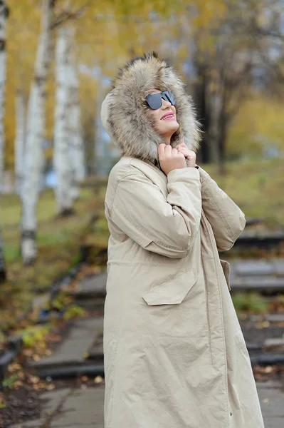 A girl in a green jacket with a fur collar in glasses posing near the lake — Stock Photo, Image