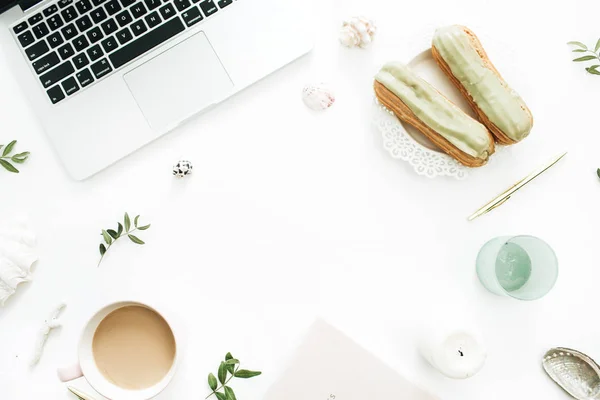 Home office desk frame with laptop, pistachio cakes, coffee mug, leaves, sea shells on white background. Flat lay, top view still life concept.