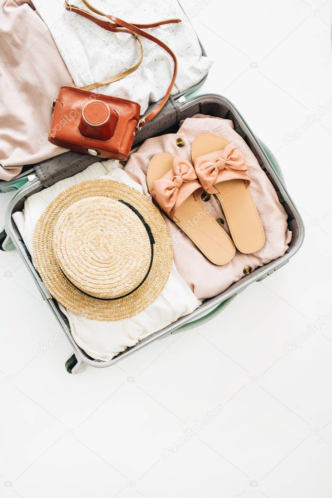 Hand luggage with stylish woman's clothes and retro camera on white background. Flat lay, top view. Summer fashion and travel concept.