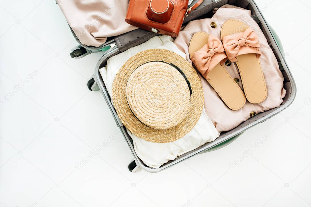 Hand luggage with stylish female clothes and retro camera on white background. Flat lay, top view. Summer fashion travel concept.