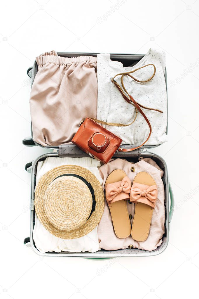 Hand luggage with stylish female clothes on white background. Flat lay, top view. Summer travel fashion concept.