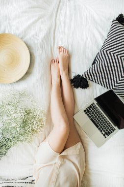 Yatakta dizüstü bilgisayarda çalışan genç kadın. Yaşam tarzı kompozisyon yukarıdan manzaralı beyaz çiçekler Buket, yastık ve ahşap plaka ile dekore edilmiştir. Serbest meslek ya da blogger ev çalışma alanı kavramı.