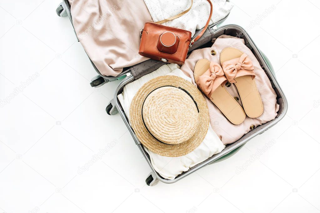 Hand luggage with stylish female clothes and retro camera on white background. Flat lay, top view. Summer fashion clothes and travel concept.